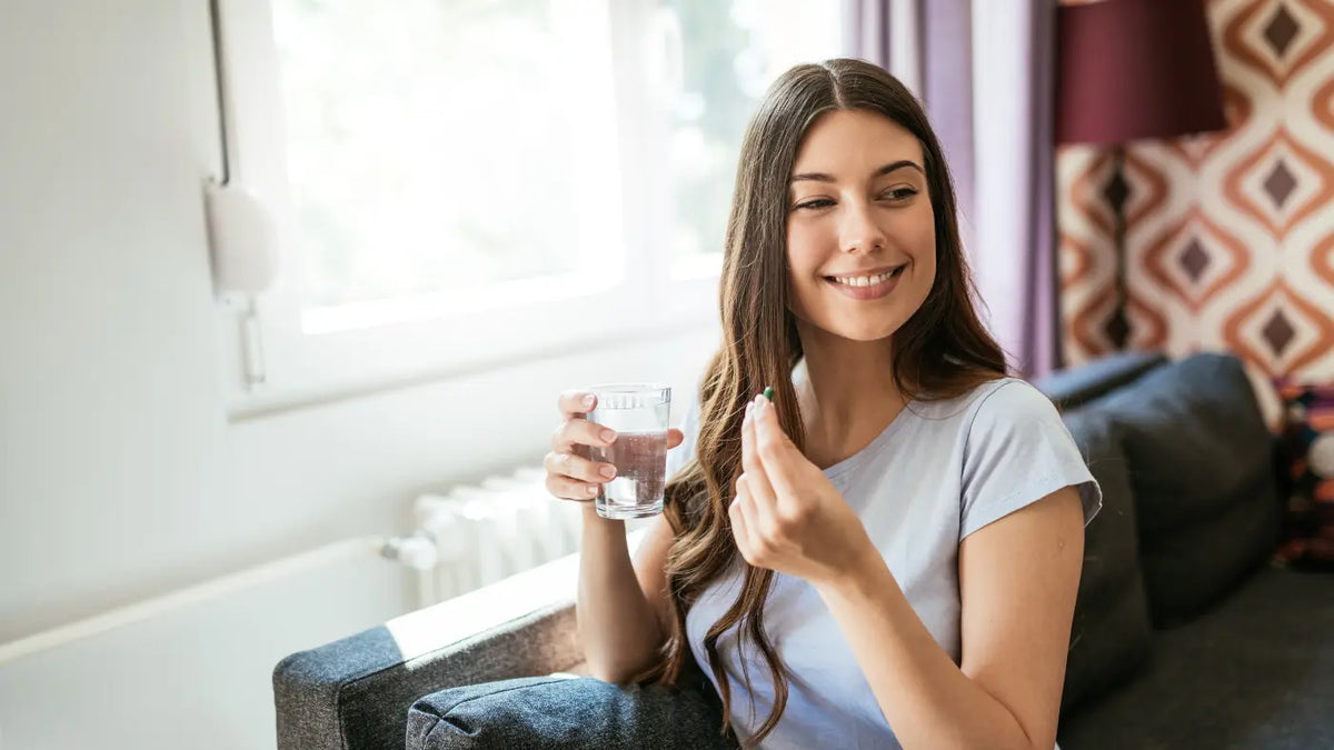 Brünette lächelnde Frau hält Nahrungsergänzung und ein Glas Wasser in den Händen