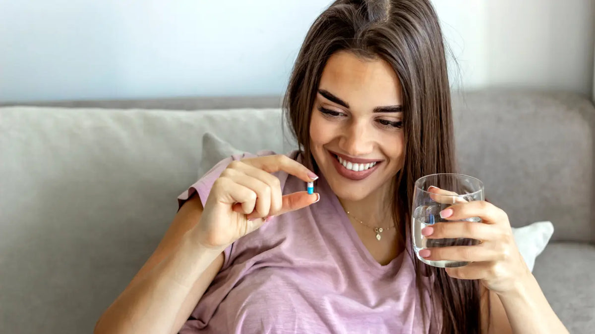 Brünette lächelnde Frau hält Supplement und Glas Wasser in den Händen